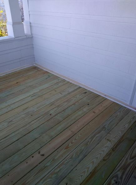 View of an empty wooden deck area with light-colored planks and white walls.