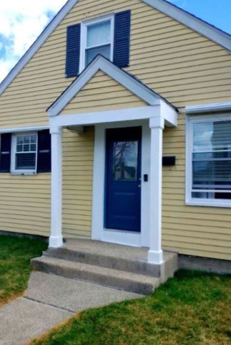 Yellow house with blue front door, white columns, and blue shutters on windows.