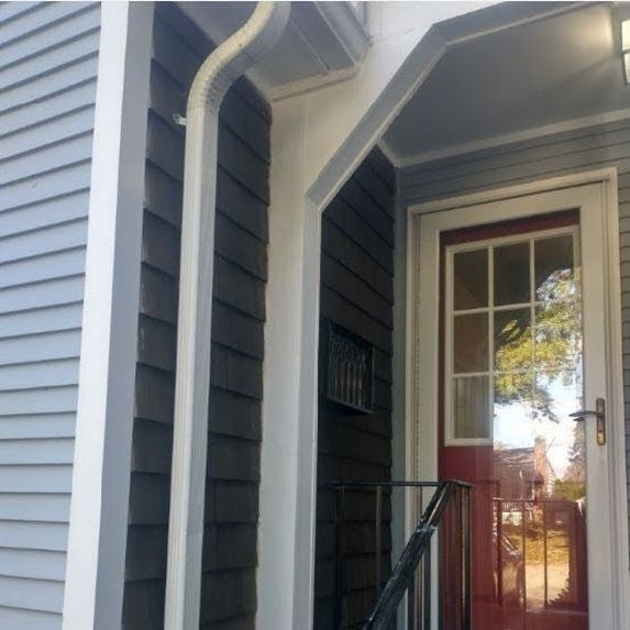 Front door with glass panels and red trim, surrounded by grey siding and a small porch.