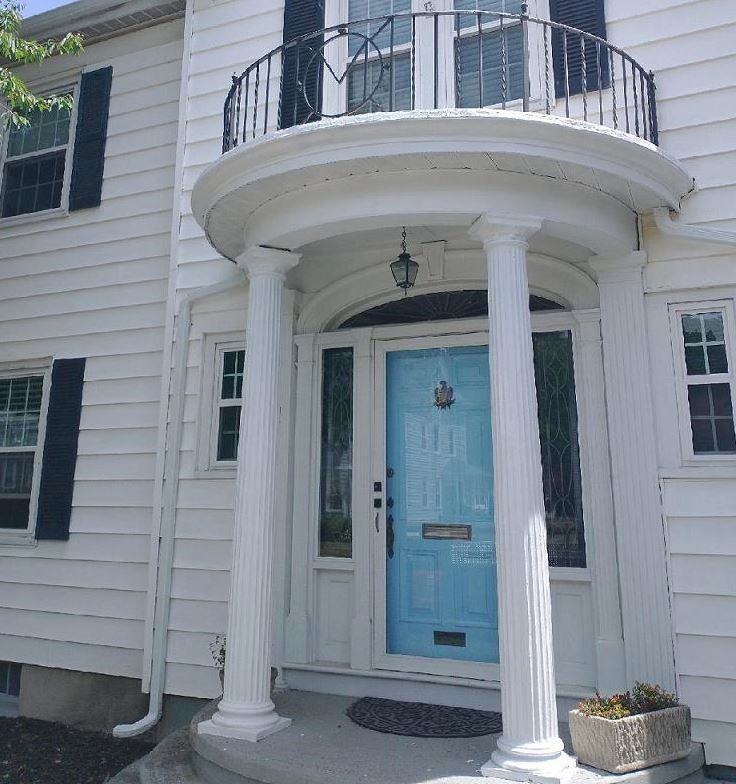 Front entrance of a house with a blue door, white columns, and a small balcony above.