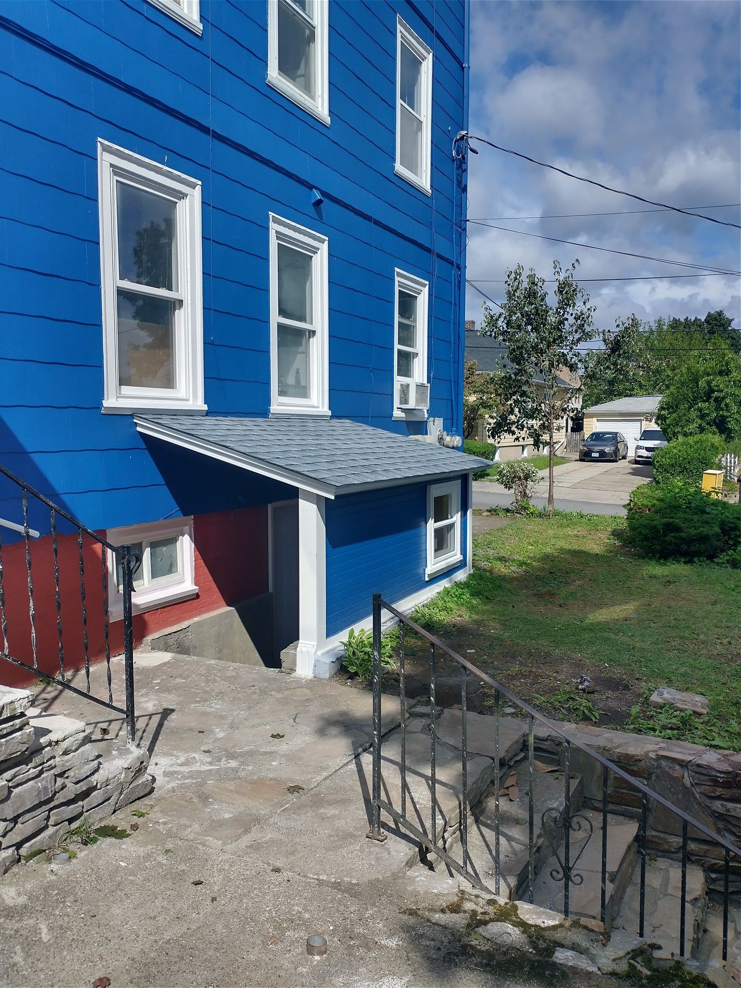 Blue multi-story house with multiple windows, small porch, and stone steps leading to a garden.